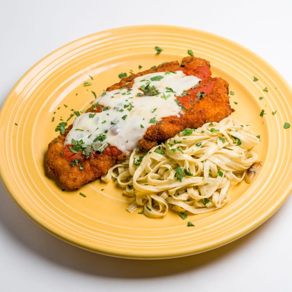 Chicken parmesan with melted cheese and red sauce, alongside fettuccine pasta, on a yellow plate.