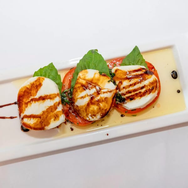 Three Caprese salad servings, with mozzarella, tomato, basil, and balsamic glaze on a white plate.