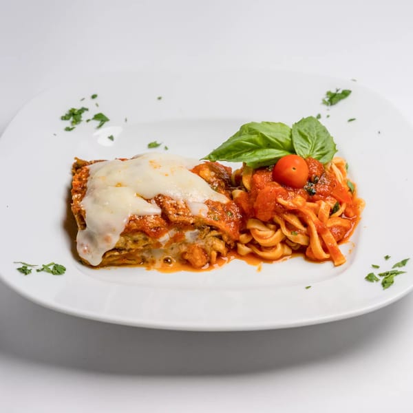 A slice of lasagna with melted cheese and a side of pasta with tomato sauce and basil.