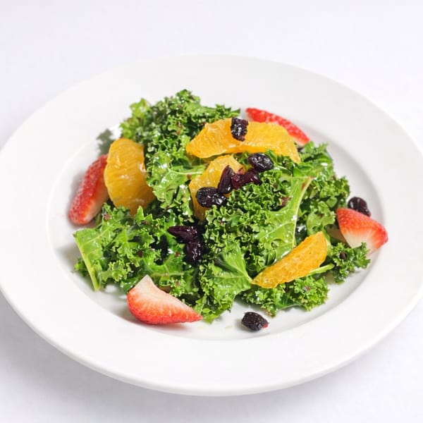 Kale salad with orange slices, strawberries, and dried cranberries on a white plate.