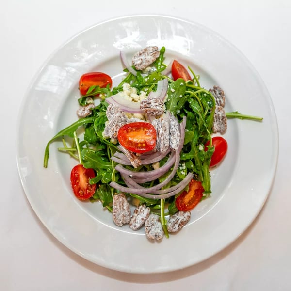 A vibrant Roma Restaurant salad with arugula, cherry tomatoes, red onion, blue cheese, and candied pecans.