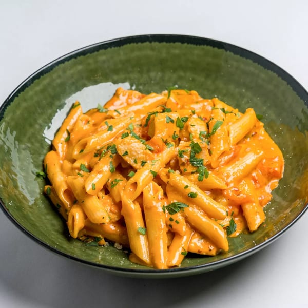Penne pasta with creamy orange sauce, chicken, and parsley in a dark green bowl.