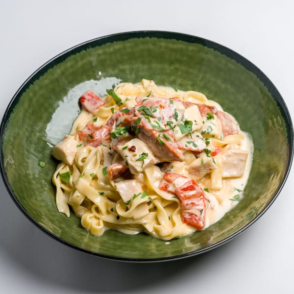 Creamy fettuccine pasta with chicken, red bell peppers, and parsley in a green bowl.