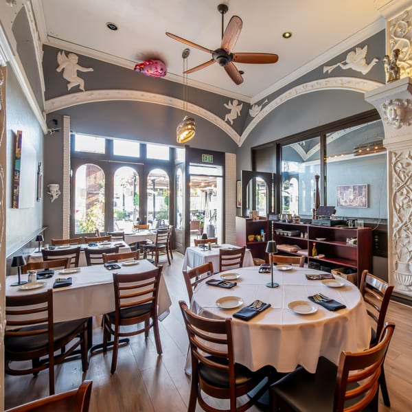 Elegant dining room at Roma Restaurant with white-clothed tables, wooden chairs, and decorative cherub accents.