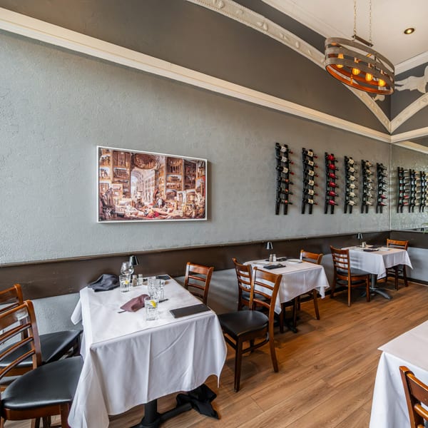 Interior of Roma Restaurant with set tables, wine racks, and a large framed artwork on the wall.