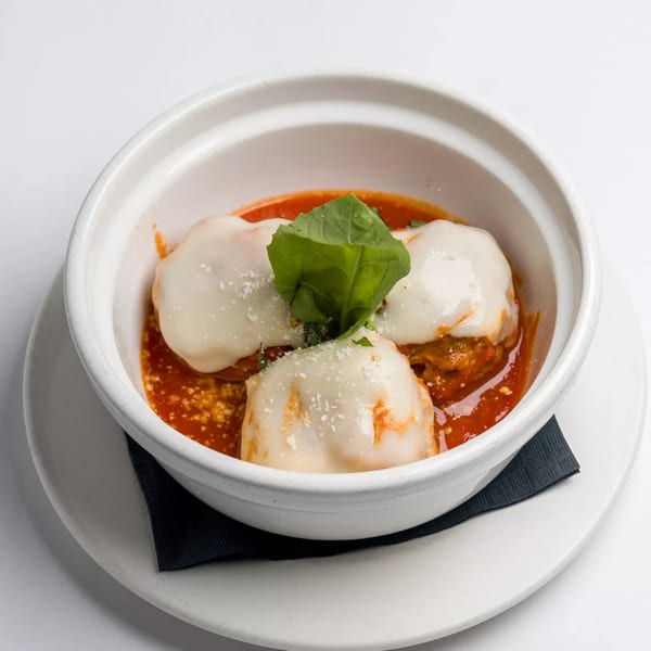 Three meatballs covered in melted mozzarella cheese, tomato sauce, and fresh basil in a white bowl.