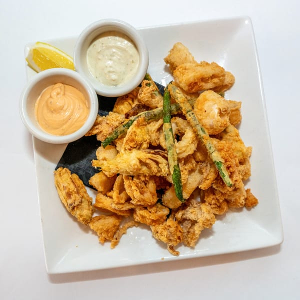 Fried calamari and green beans with two dipping sauces and a lemon wedge on a white plate.