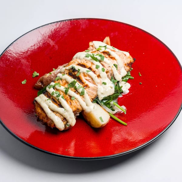 Grilled chicken with creamy sauce and fresh herbs, served on a bed of greens on a red plate.