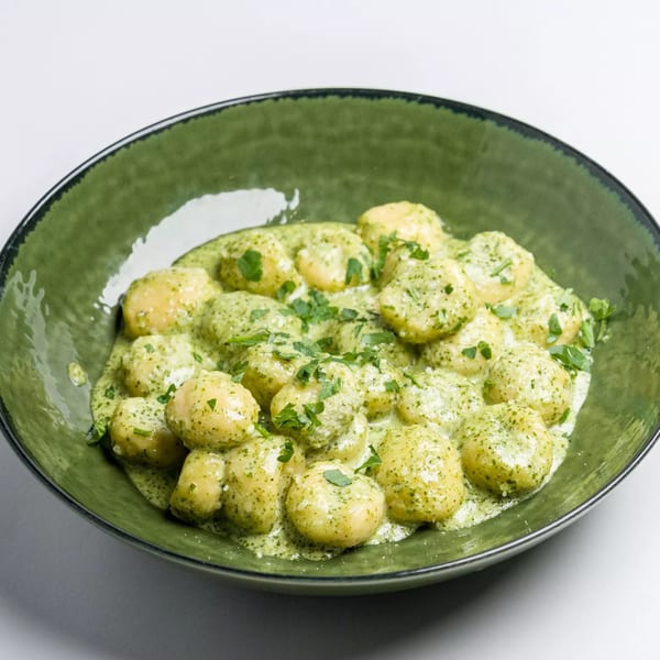 A green bowl filled with Italian gnocchi in a creamy pesto sauce, garnished with fresh parsley.
