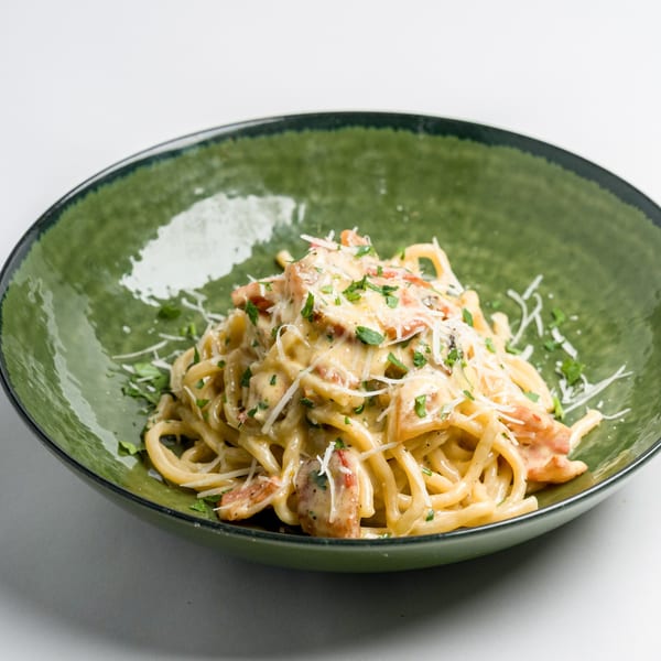 Creamy spaghetti carbonara with bacon, parmesan, and parsley in a green bowl.
