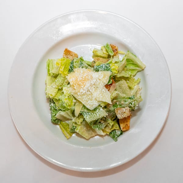 A Caesar salad with romaine lettuce, croutons, and parmesan cheese on a white plate.