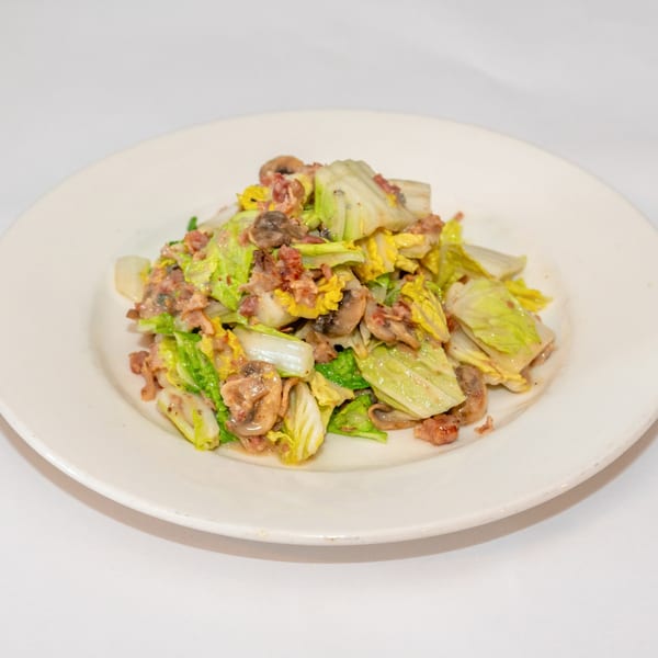 A white plate holds a serving of sautéed cabbage, mushrooms, and bacon bits.
