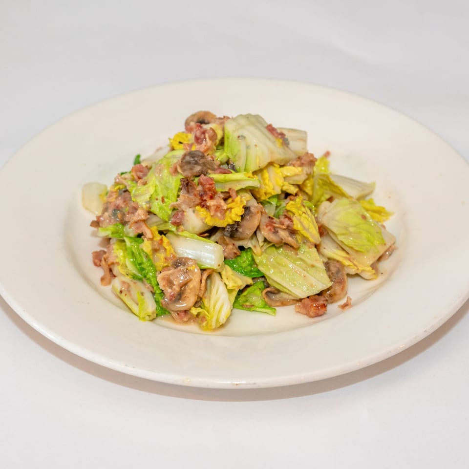 A white plate holds a serving of sautéed cabbage, mushrooms, and bacon bits.
